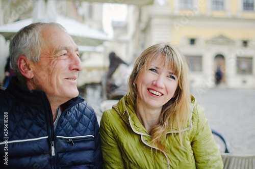 Handsome elderly man is embracing his young blonde wife spending time together outdoors in the ancient city during early spring or autumn.