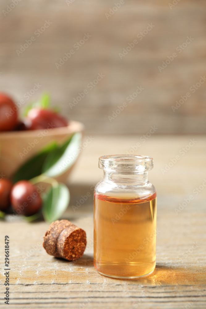 Glass bottle with jojoba oil on wooden table Glass bottle with jojoba oil on wooden table