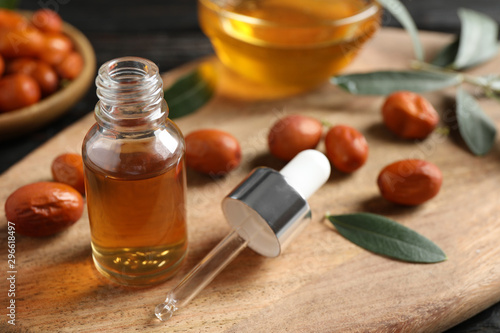 Glass bottle with jojoba oil and seeds on wooden board