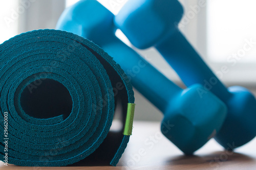 A blue rolled yoga mat. Two blue 2 kg dumbells resting on it. Fitness equipment for home exercise and flexibility training. photo