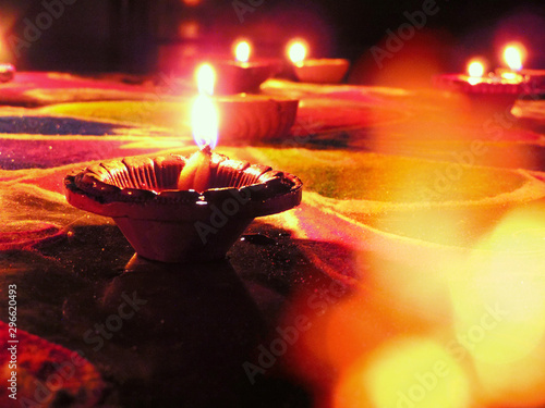 low angle shot of diwali oil clay lamps with intricate red green colored design placed on multicoloured rangoli background