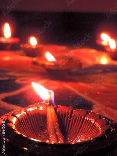 Close up of four Diwali oil clay lamps with intricate red green colored design placed in a row and diagonally on multicolored rangoli background
