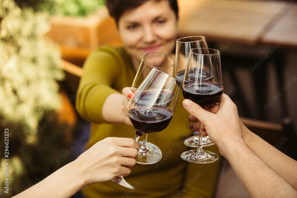 People clinking glasses with wine on the summer terrace of cafe or restaurant. Happy cheerful friends celebrate summer or autumn fest. Close up shot of human hands, lifestyle. People clinking glasses with wine on the summer terrace of cafe or restaurant. Happy cheerful friends celebrate summer or autumn fest. Close up shot of human hands, lifestyle.