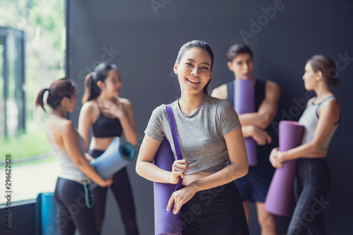 Asian cute woung girl stand in the front Group of mix race of Caucasian and Asian sporty people both women and men talk and Laugh at black wall waiting for enjoy yoga class together