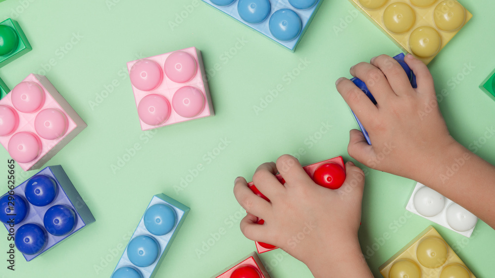 Toy bricks. Kid's hands with blocks toy on green background. Educational toy, flat lay, top view. Toy bricks. Kid's hands with blocks toy on green background. Educational toy, flat lay, top view.