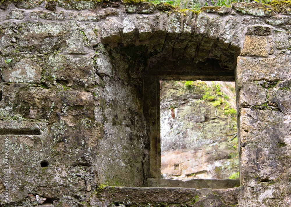 view through a window in the wall of the ruins of an old water mill made of natural stone in the forest near Dolny Mlyn in Bohemian Switzerland national park