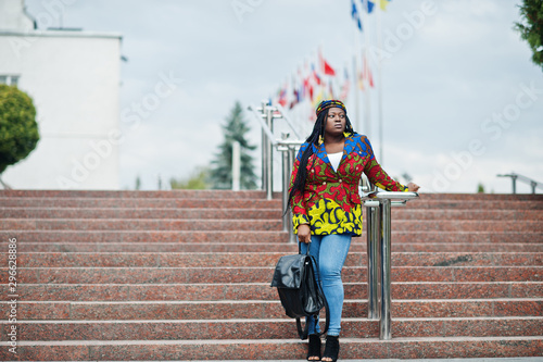 African student female posed with backpack on yard of university, against flags of different countries.
