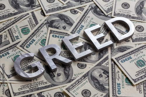 Obraz na plátně The word GREED laid with aluminium letters on the US dollar banknotes background