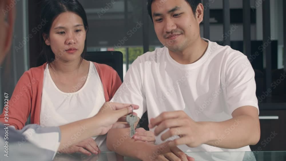 Young Asian Pregnant couple sign contract documents at home, Japanese family consulting with real estate financial advisor, Buying new house and handshaking with broker giving keys in living room. Young Asian Pregnant couple sign contract documents at home, Japanese family consulting with real estate financial advisor, Buying new house and handshaking with broker giving keys in living room.