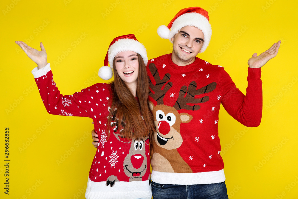 Beautiful man and woman in christmas sweaters and santa hats on yellow background Beautiful man and woman in christmas sweaters and santa hats on yellow background