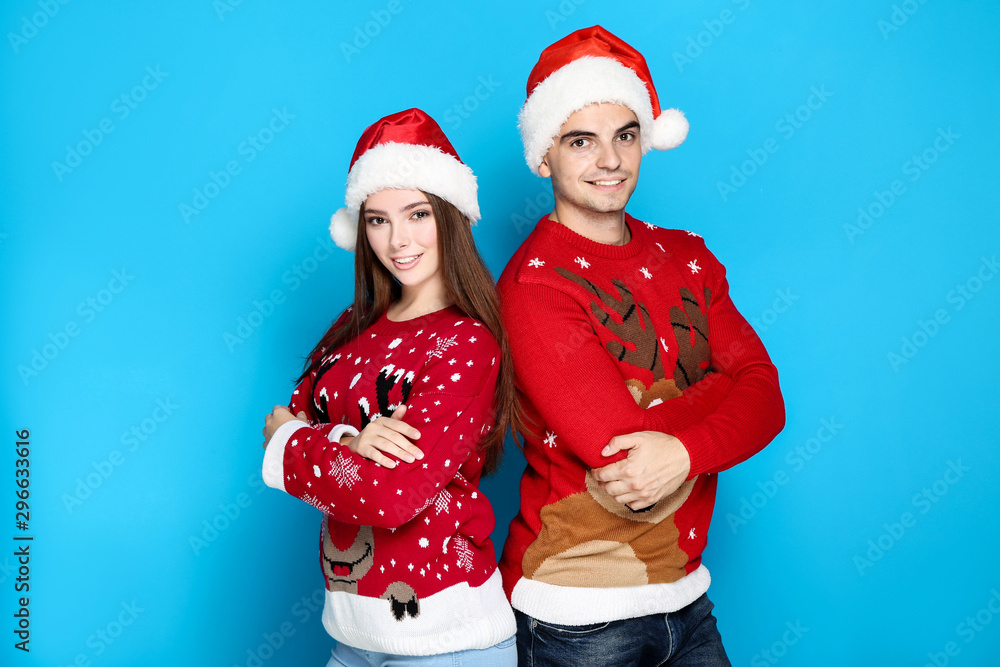 Beautiful man and woman wearing christmas sweaters and santa hats on blue background Beautiful man and woman wearing christmas sweaters and santa hats on blue background