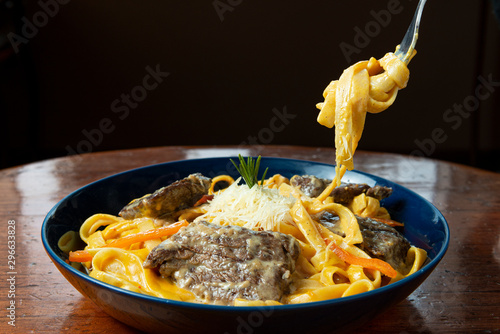 Fork holding noodles with meat and cheese. Fetucinni with huancaina, cheese and grilled beef. Wooden background. photo