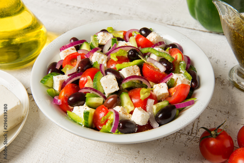 Traditional Greek salad in a round white salad bowl on an white wooden table. Selected focus. Traditional Greek salad in a round white salad bowl on an white wooden table. Selected focus.