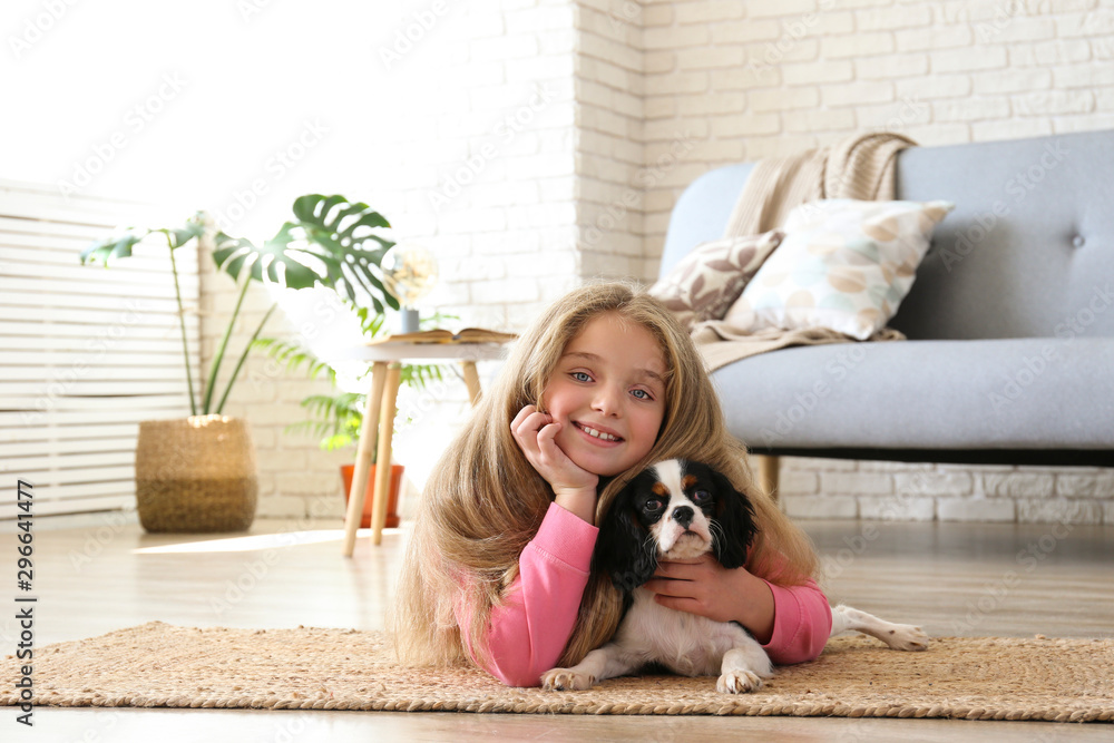 Portrait of little girl with long blonde straight hair playing with black and white Cavalier King Charles Spaniel puppy at home. Child with her pet friend. Lofty interior design. Close up, copy space. Portrait of little girl with long blonde straight hair playing with black and white Cavalier King Charles Spaniel puppy at home. Child with her pet friend. Lofty interior design. Close up, copy space.