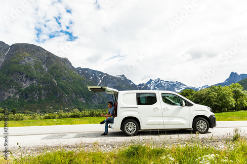 Young travel man sitting in car trunk typing on phone with beauty nature landscape on background