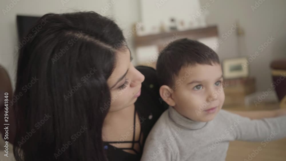 Portrait of a smiling Middle Eatern boy with hazel eyes imitating airplane flight. Cheerful mother playing with her little son at home. Camera moving dynamically following people. Portrait of a smiling Middle Eatern boy with hazel eyes imitating airplane flight. Cheerful mother playing with her little son at home. Camera moving dynamically following people.