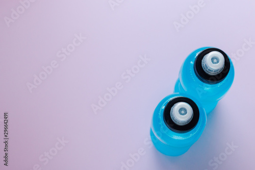 Two bottles of blue clear liquid, sports energy drink on a pink background. Selective focus