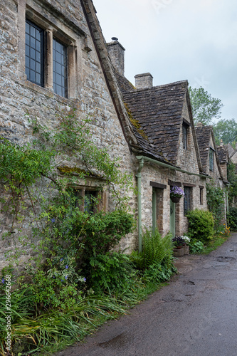 BIBURY, COTSWOLDS, UK - MAY 28, 2018: Traditional cotswold stone cottages built of distinctive yellow limestone in the world famous Arlington Row, Bibury, Gloucestershire, England 