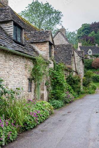 BIBURY, COTSWOLDS, UK - MAY 28, 2018: Traditional cotswold stone cottages built of distinctive yellow limestone in the world famous Arlington Row, Bibury, Gloucestershire, England   