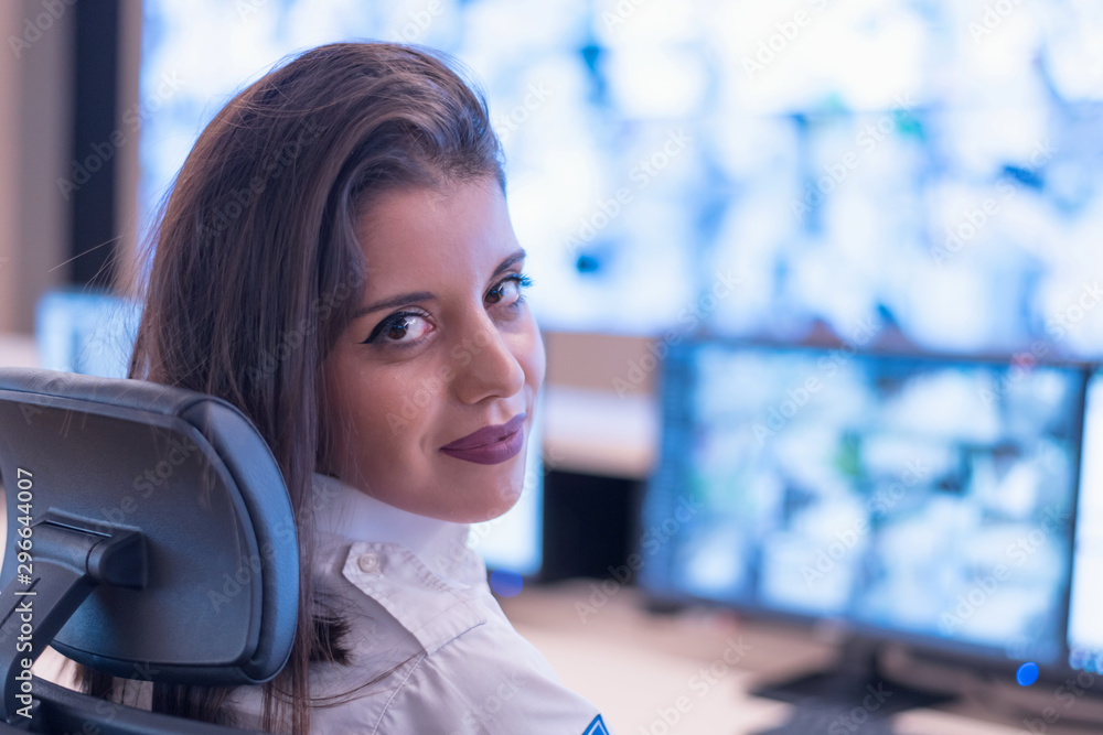 Security guard monitoring modern CCTV cameras in surveillance room. Female security guard in surveillance room. Smiling into camera. Security guard monitoring modern CCTV cameras in surveillance room. Female security guard in surveillance room. Smiling into camera.