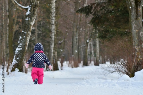 little girl walking in the snowy winter park. Back view.