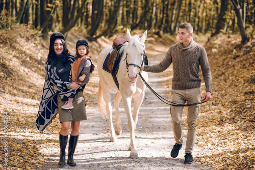 Young family is learning to ride a beautiful white horse in the autumn forest. Riding lesson © Олег Кошевський