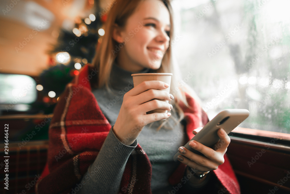 Φωτογραφία Closeup photo, smiling girl holding a cup of coffee and smartphone in her hand, focus on a paper cup with coffee