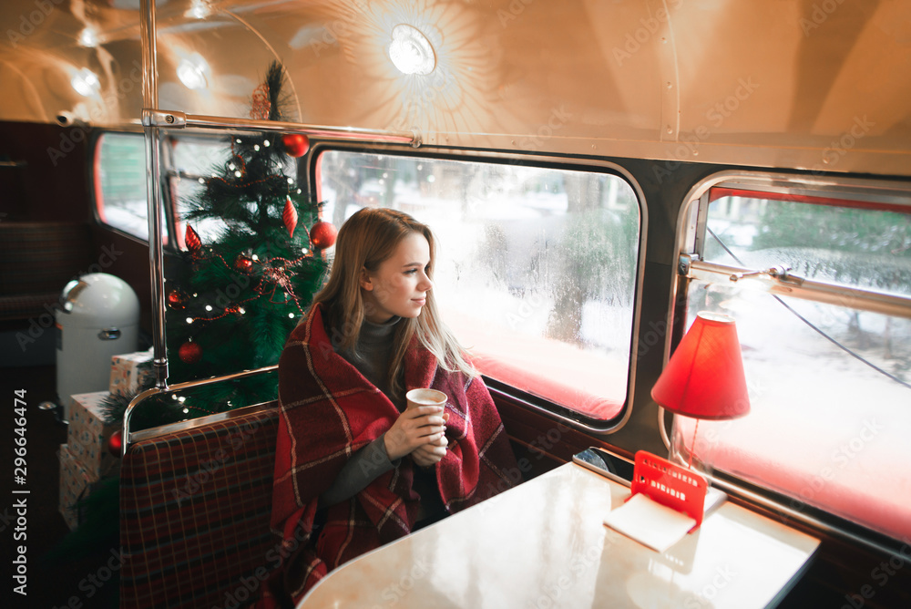 Φωτογραφία Beautiful girl in plaid and with a cup of hot drink sits in a cafe on a cold winter day on the background of a Christmas tree, looking thoughtfully out the window