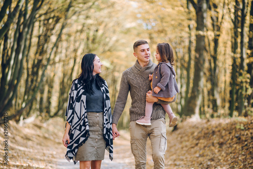 Beautiful young family walking in the autumn forest. Family walking in an autumn park with fallen fall leaves. Warm autumn