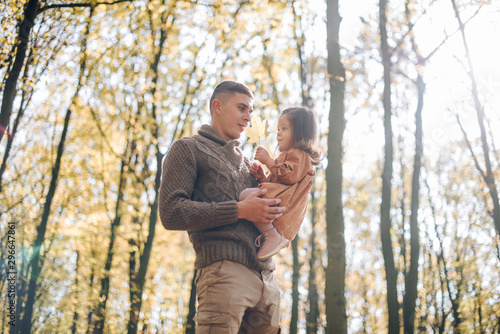 Family autumn weekend. Young father and his little daughter together in autumn park outdoors. Beautiful baby with leaves on top of dad. © Олег Кошевський