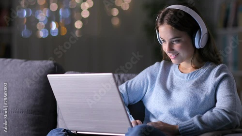 Concentrated woman wearing headphones writing on laptop sitting on a couch in the 