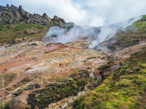 Colorful rhyolit red, orange and yellow fumarole at Reykjadalur valley with sharp rocks, grass meadow and geothermal steam. South Iceland near Hveragerdi city. Summer sunny day photo