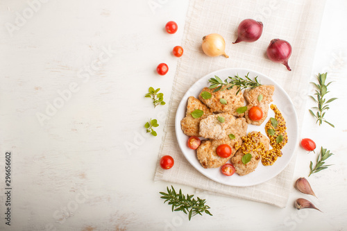 Fried pork chops with tomatoes and herbs on a white ceramic plate on a white wooden background. top view, copy space.