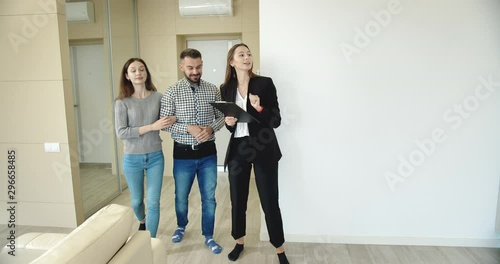Lady real estate manager showing young man and woman apartment, family searching new home