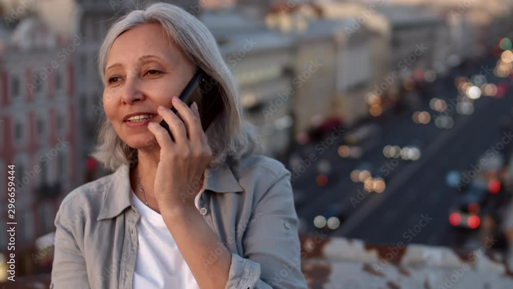 Close up portrait of mixed-race woman with grizzle hair sitting on roof in downtown with smartphone in her hands and having chat Close up portrait of mixed-race woman with grizzle hair sitting on roof in downtown with smartphone in her hands and having chat