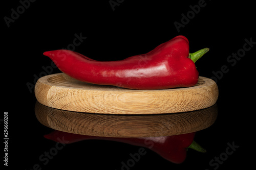 One whole sweet red bell pepper on bamboo plate isolated on black glass