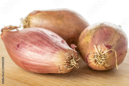 Group of three whole fresh brown shallot on bamboo cutting board isolated on white background