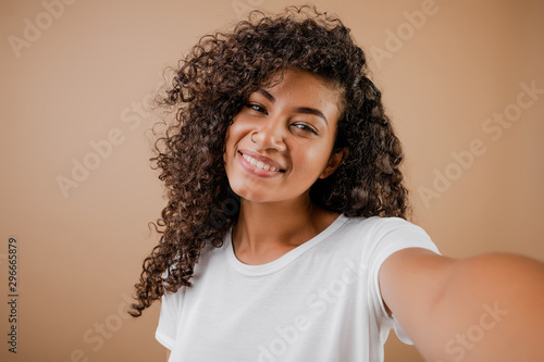 lovely happy black young woman making selfie isolated over brown photo