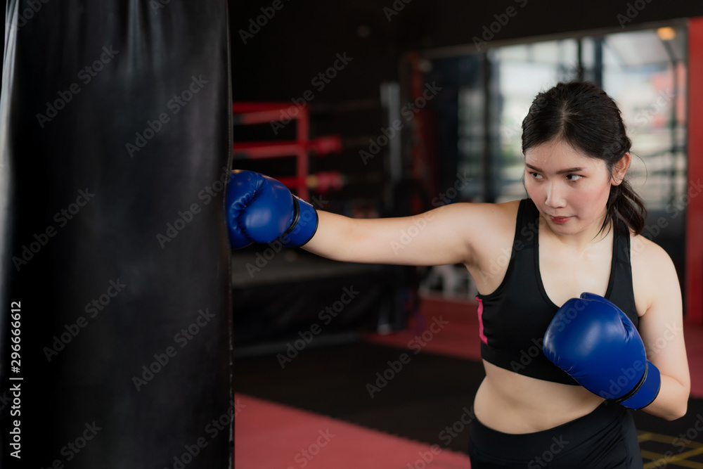 Portrait of Asian confident young boxer woman with blue boxing gloves, punching a Bag in professioal gym. Sporty fit for healthy lifestyle Asian model of boxing gym concept..
