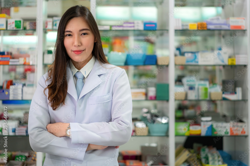 Confident Asian young female pharmacist with a lovely friendly smile standing with folded arms in the pharmacy drugstore. Medicine, pharmaceutics, health care and people concept.