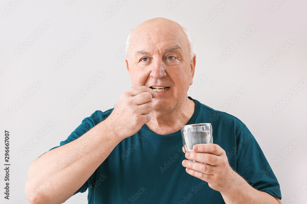 Elderly man taking medicine on light background Elderly man taking medicine on light background