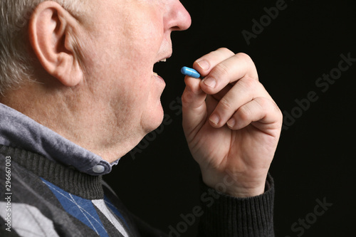 Elderly man taking pill on dark background, closeup