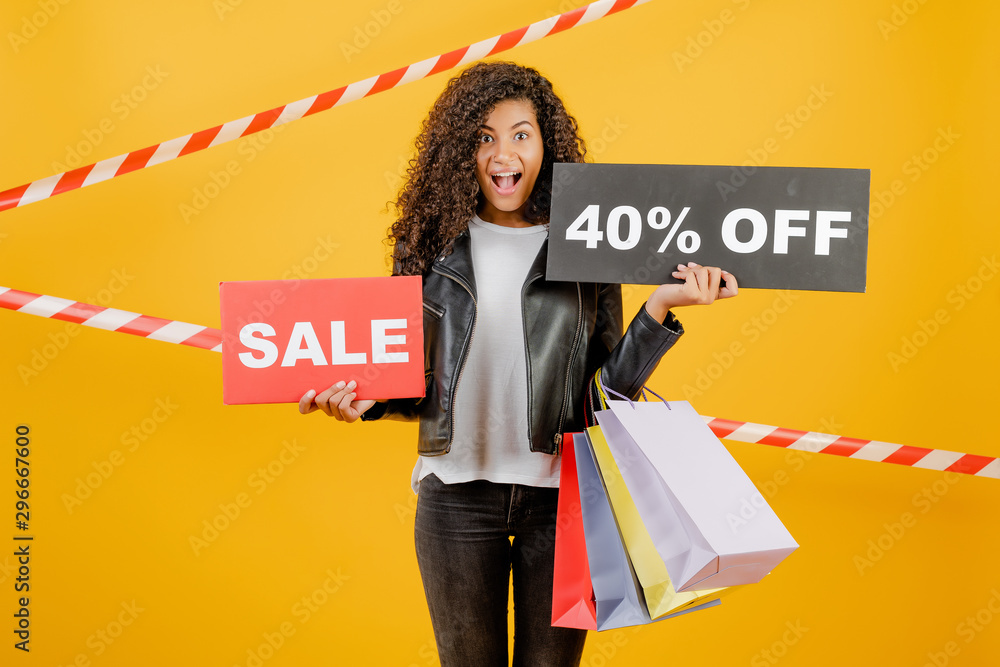 trendy young black girl with sale 40% sign and colorful shopping bags isolated over yellow with signal tape trendy young black girl with sale 40% sign and colorful shopping bags isolated over yellow with signal tape