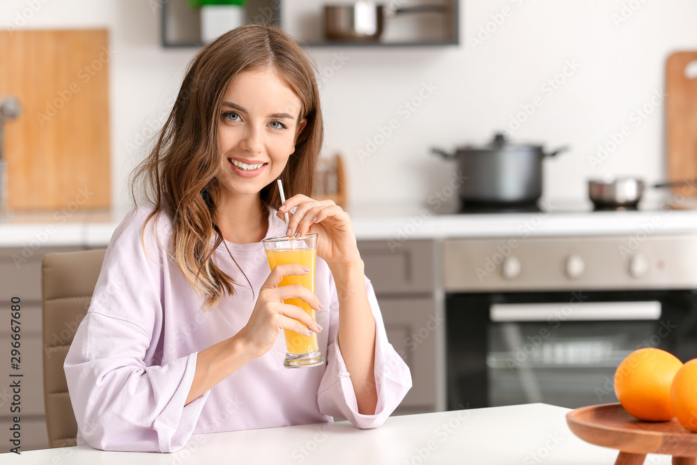 Beautiful young woman drinking orange juice in kitchen