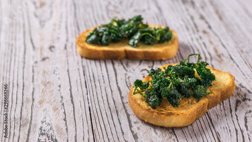 Two slices of fried bread with fried greens on a wooden table.