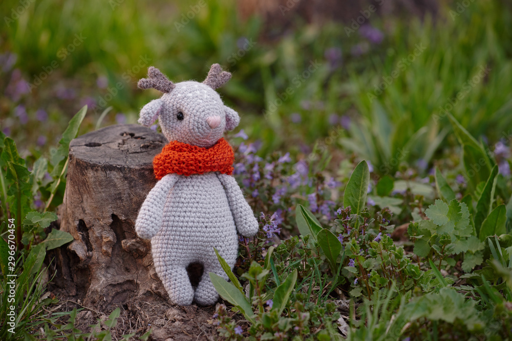 Beautiful handmade soft toy fawn. Outdoor photography, grass and a small stump. Beautiful handmade soft toy fawn. Outdoor photography, grass and a small stump.
