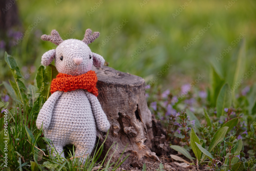 Beautiful handmade soft toy fawn. Outdoor photography, grass and a small stump.