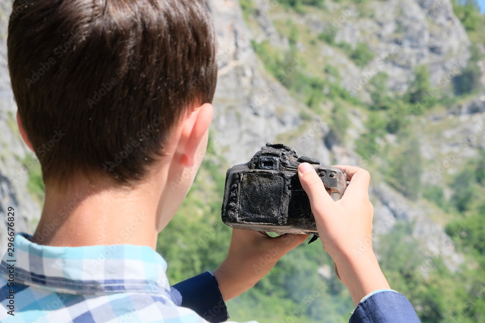 How to take pictures of a burned-out device. A molten charred SLR camera in the hands of a teenager. The tropical heat ruined the camera. The concept of camera repair after extreme travel. How to take pictures of a burned-out device. A molten charred SLR camera in the hands of a teenager. The tropical heat ruined the camera. The concept of camera repair after extreme travel.
