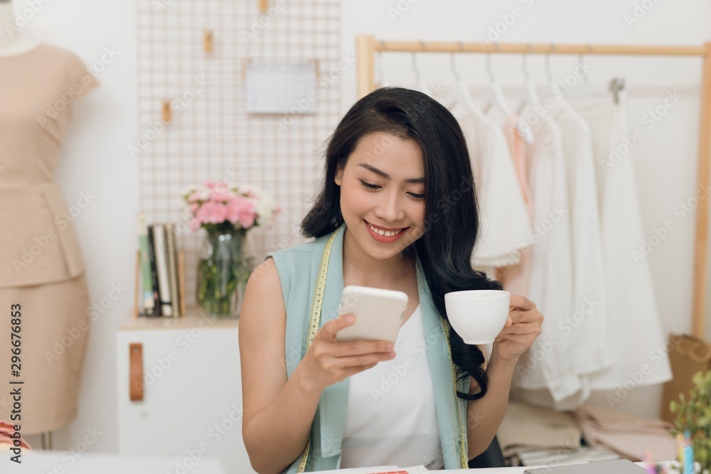 Portrait of young Asian business woman/fashion designer take a rest while drinking coffee and using mobile phone Portrait of young Asian business woman/fashion designer take a rest while drinking coffee and using mobile phone