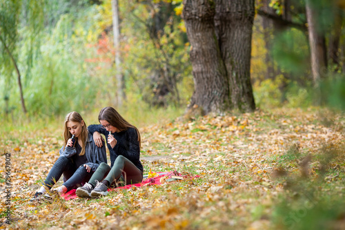 Vape lgbt teenagers. Bisexual lesbian young caucasian teenage girls in casual clothes vape electronic cigarette on the street in the park in the autumn evening. Bad habit.